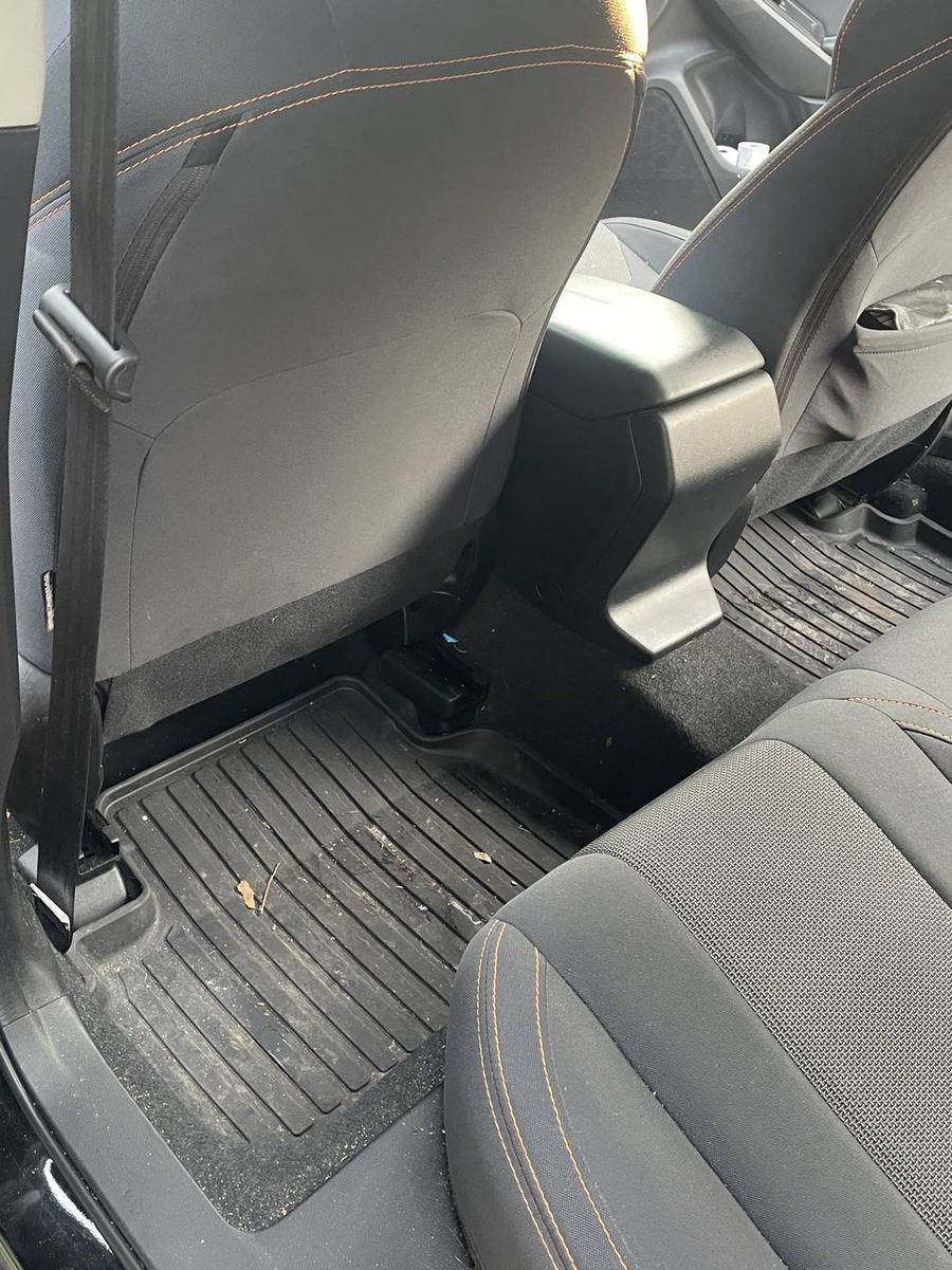 Subaru Crosstrek rear footwells before detailing — leaf litter and debris scattered across the mat